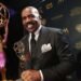Steve Harvey holding the award in black backdrop on a full suit.